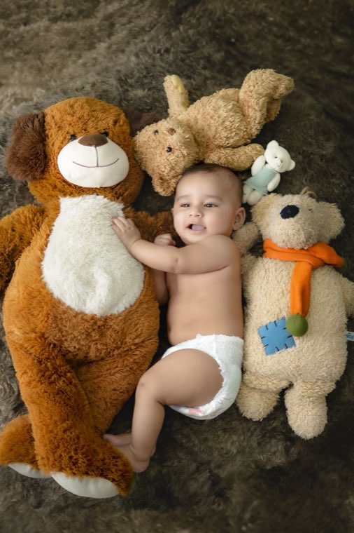 Smiling baby lying among teddy bears